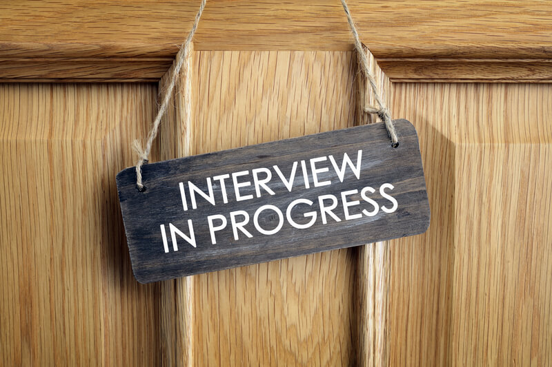 a sign saying Interview in Progress hangs on a wooden door