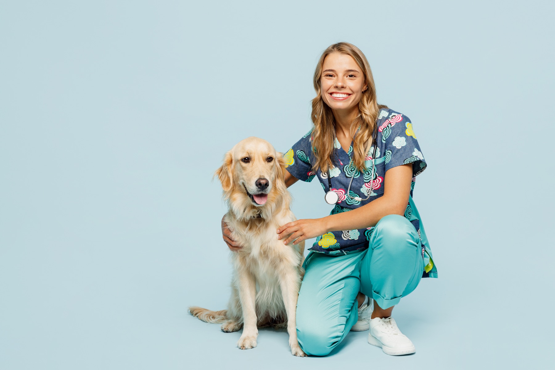 Smiling veterinary technician kneeling beside a golden retriever